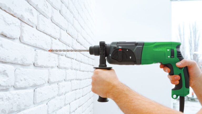 homem com uma furadeira de impacto verde furando a parede de concreto