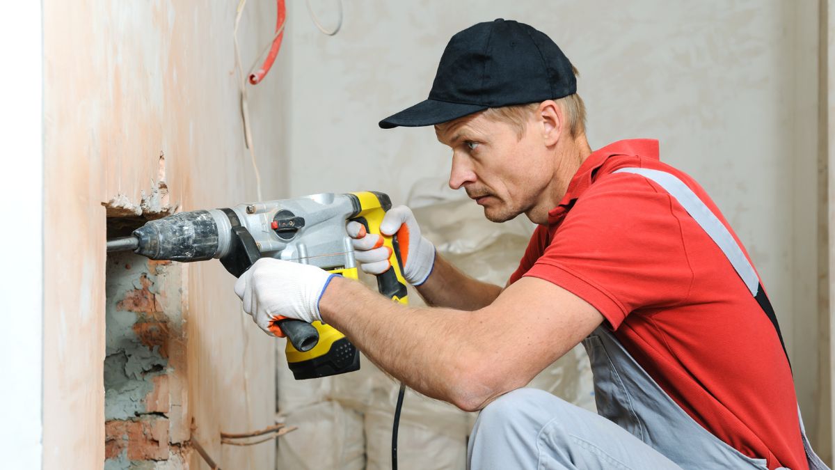 homem de vermelho e boné usando um martelete na parede